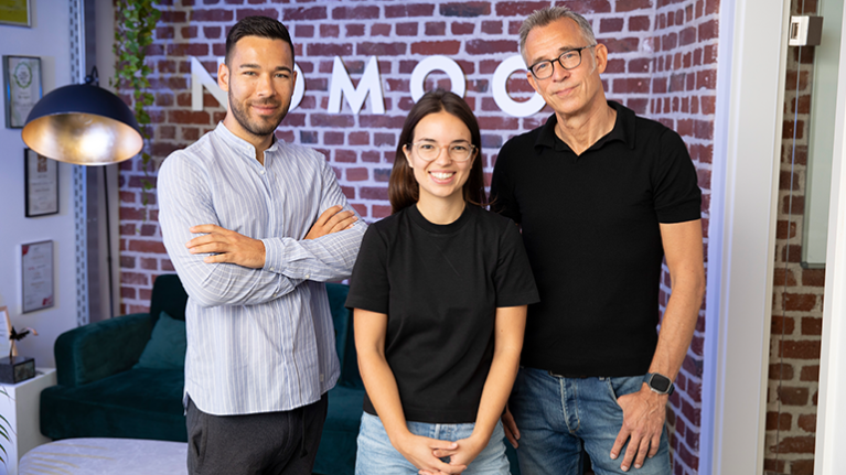 Drei Personen stehen nebeneinander vor einer Backsteinwand