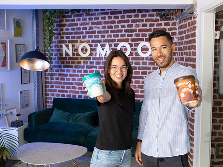 Zwei Personen; eine junge Frau und ien junger Mann, stehen vor einer Backsteinwand und halte zei Eisbecher in der Hand