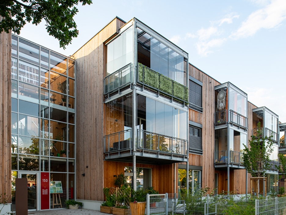 Frontansicht des Wohnprojekts TRIALOG in Hilden mit holzverkleideter Fassade und modernen Erkern aus Glas.