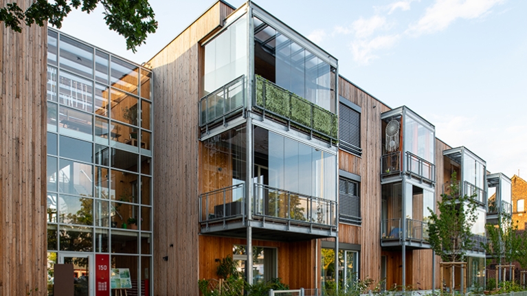 Frontansicht des Wohnprojekts TRIALOG in Hilden mit holzverkleideter Fassade und modernen Erkern aus Glas.