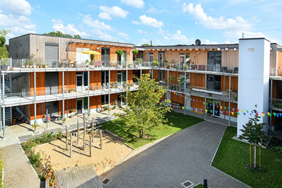 Innenhof des Wohnprojekts TRIALOG in Hilden mit Spielplatz und bunten Fahnengirlanden.