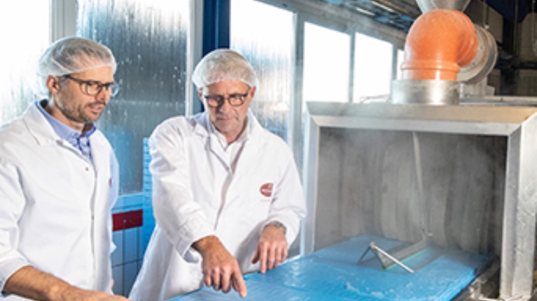 Die Geschäftsführer stehen an einer Dielenwaschanlage, die ein Förderband enthält und pro Jahr rund 300.000 Plastiktücher eingespart.