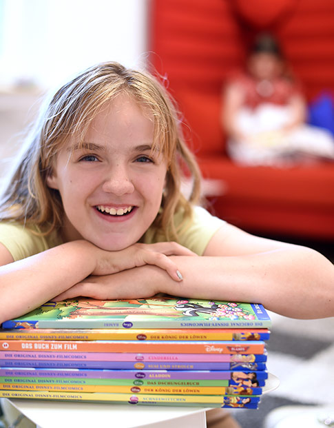 Lachendes Mädchen mit einem Stapel Kinderbücher