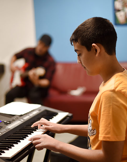Eine Junge im MANUS Kinder- und Jugendzentrum spielt Keyboard.
