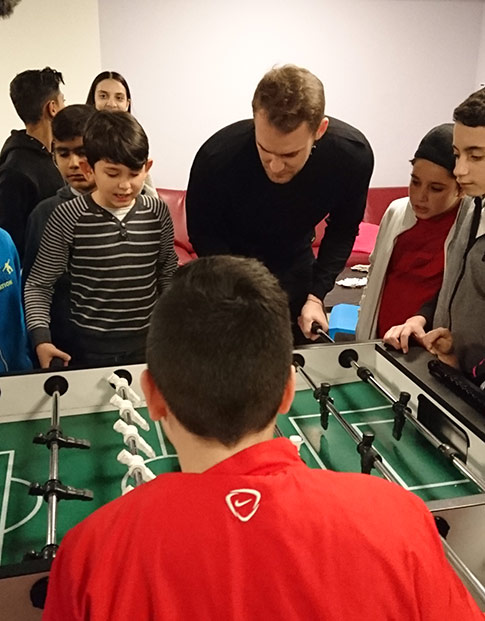 Fußballprofi Manuel Neuer spielt mit Kindern am Kicker.