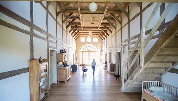 Innenraum einer zu einer Kita umgebauten Kirche mit Holzdielen und -balken. 2 Kinder spielen mit einer Katze.