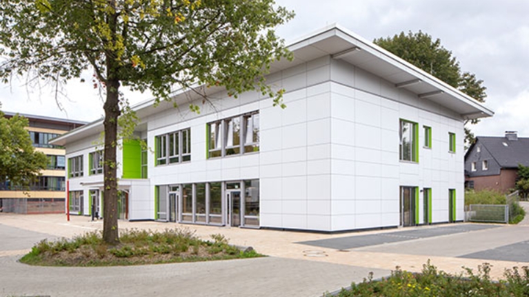 Ein Schulgebäude mit weißer Fassade und grünen Elementen
