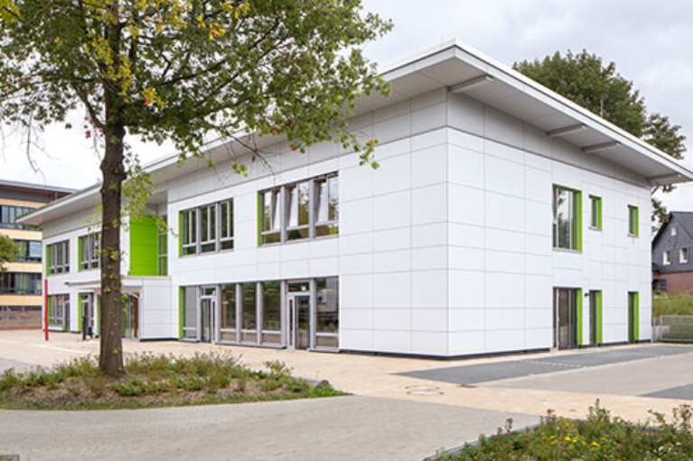 Ein Schulgebäude mit weißer Fassade und grünen Elementen