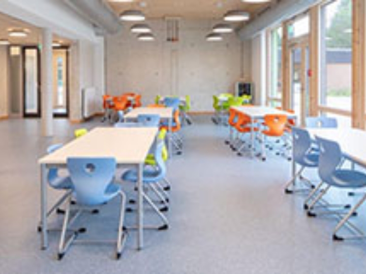 Blick in einen hellen Aufenthaltsraum in einer Schule mit bunten Stühlen und weißen Tischen.