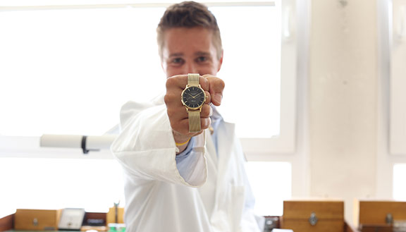 Ein junger Mann hält eine goldene Uhr in die Kamera.