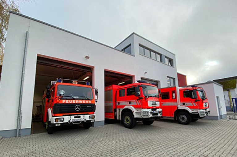 Drei Feuerwehrautos stehen in den Einfahrten eines Feuerwehrhauses