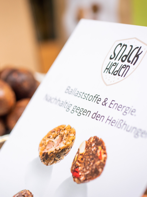 Eine Schale mit den kugelförmigen Snacks der Snackhelden. Davor eine Karte mit dem Logo des Unternehmens.