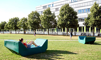 Wiese mit Bäumen und Studierenden, im Hintergrund ein Gebäude der Universität Bielefeld