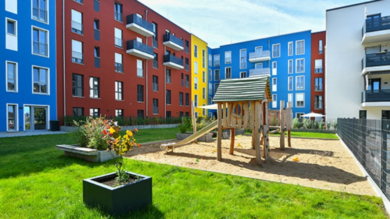 Bunte Hausfassaden umschließen ein Innenhof mit Spielplatz und Grünfläche
