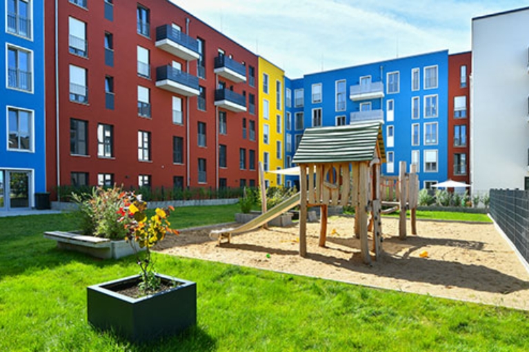 Bunte Hausfassaden umschließen ein Innenhof mit Spielplatz und Grünfläche