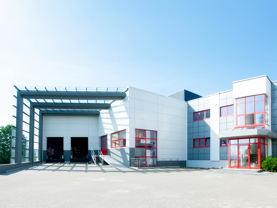 Weißes Gebäude mit roten Fensterelementen und zwei großen Toren zur Mashinenhalle