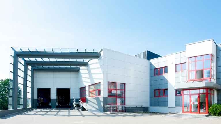 Weißes Gebäude mit roten Fensterelementen und zwei großen Toren zur Mashinenhalle