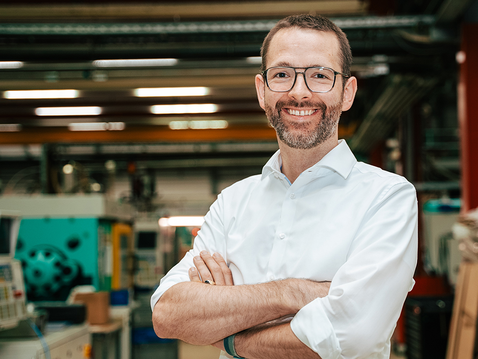 Mann mit verschränkten Armen in weißem Hemd steht in einer Lagerhalle