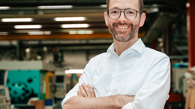 Mann mit verschränkten Armen in weißem Hemd steht in einer Lagerhalle