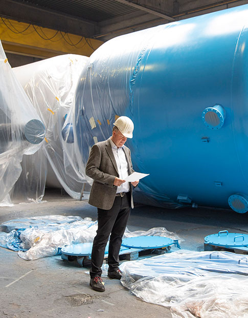 Dr. Jörg Doege, Geschäftsführer von InproCoat, in einer Halle vor einem großen blauen Metalltank