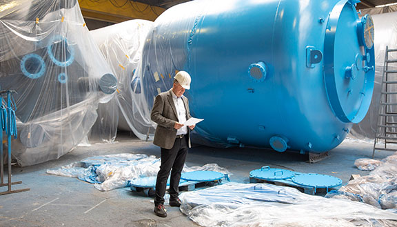 Dr. Jörg Doege, Geschäftsführer von InproCoat, in einer Halle vor einem großen blauen Metalltank