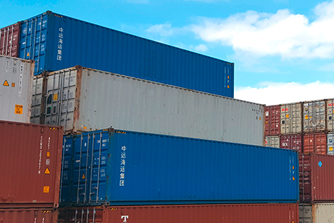 Mehrere verschiedenfarbige Schiffscontainer, die in einem Hafen gestapelt sind.