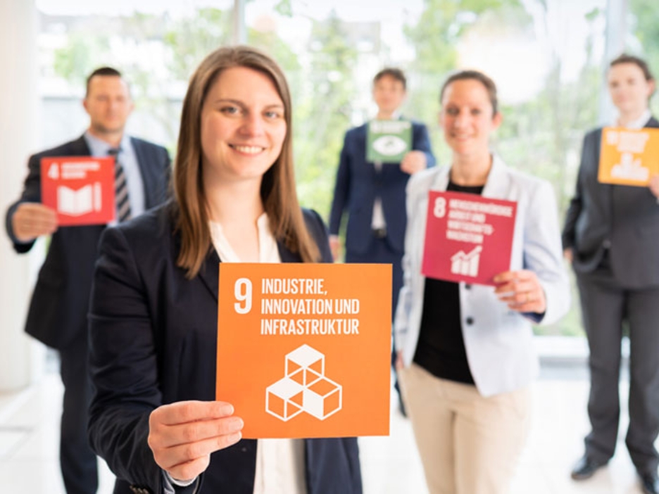 Mehrere Menschen halten Karten in die Kamera, nur die vorderste ist lesbar: Industrie, Innovation und Infrastruktur