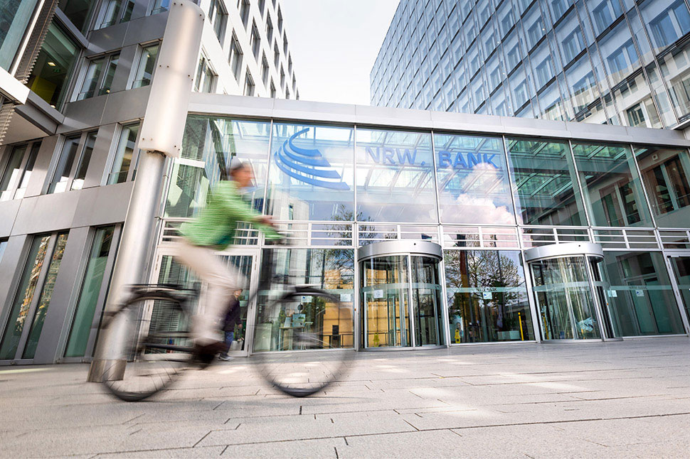 Fahrradfahrerin vor dem gläsernen Eingangsbereich der NRW.BANK-Zentrale in Düsseldorf