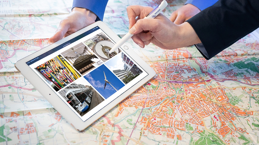 Auf einer Landkarte liegt ein Tabletcomputer, darauf Fotos verschiedener Förderprojekten der NRW.BANK