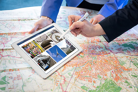 Auf einer Landkarte liegt ein Tabletcomputer, darauf Fotos verschiedener Förderprojekten der NRW.BANK