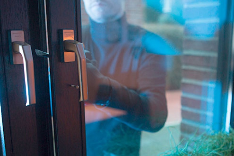 Ein dunkel gekleideter Einbrecher öffnet ein Fenster.