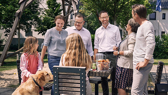 Zwei Männer, eine Frau, zwei Mädchen und ein Hund beim Picknick im Freien an einem Holztisch