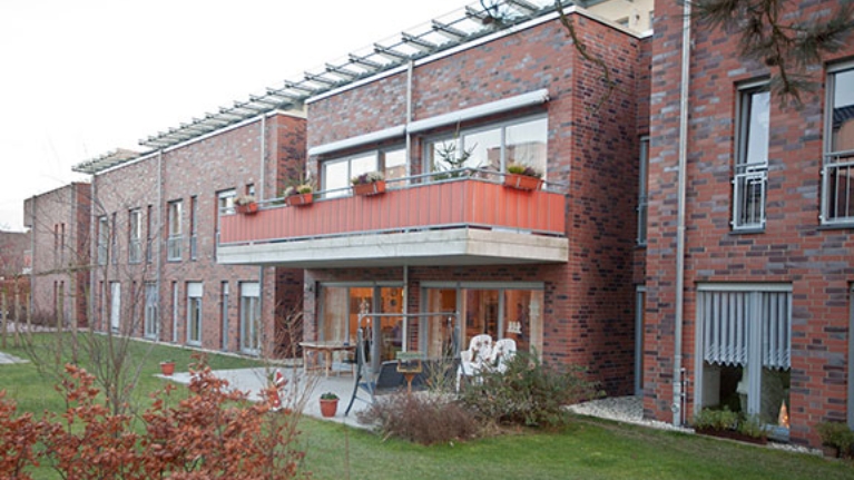 Reihenhäuser mit roter Backsteinfassade, davor Terrassen und Gärten