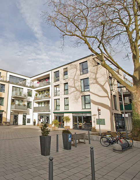 Modernes Wohnquartier mit Innenhof. Im Erdgeschoss ein Cafe, im Hof ein großer Baum und Fahrräder