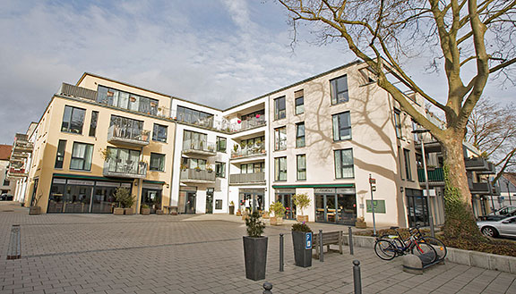 Modernes Wohnquartier mit Innenhof. Im Erdgeschoss ein Cafe, im Hof ein großer Baum und Fahrräder