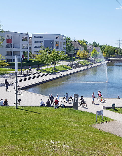 Der Niederfeldsee in Essen-Altendorf mit umliegender Parkanlage, mehreren Passanten und einem Wohnquartier