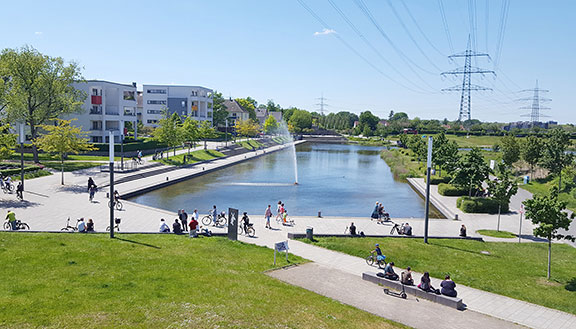 Der Niederfeldsee in Essen-Altendorf mit umliegender Parkanlage, mehreren Passanten und einem Wohnquartier