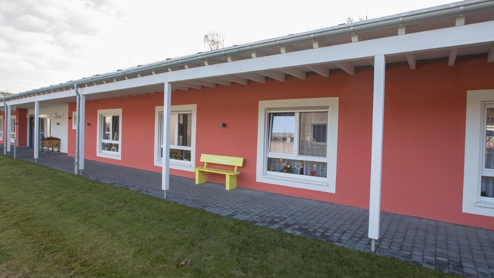 Eingeschossiges, rotes Gebäude des Seniorenzentrums Süssendell in Stolberg, davor eine gelbe Bank und eine Wiese