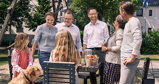 Drei Männer, zwei Frauen, zwei Mädchen und ein Hund beim Picknick im Freien an einem Holztisch