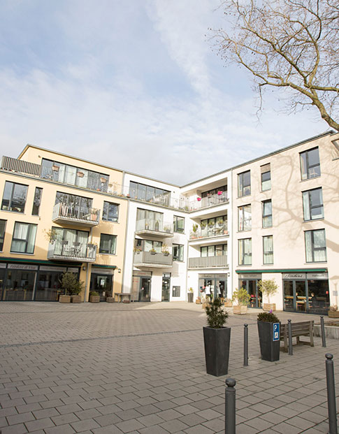 Modernes Wohnquartier mit Innenhof. Im Erdgeschoss ein Cafe, im Hof ein großer Baum und Fahrräder