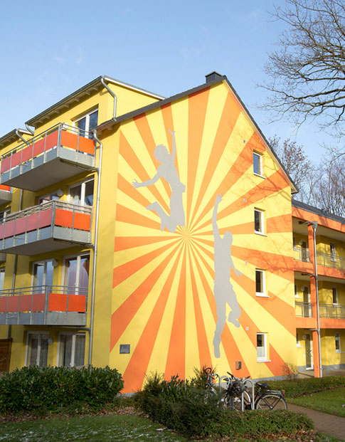 Orange-gelbe Fassade eines Studentenwohnheims mit aufgeklebten Silhouetten von Sportlern