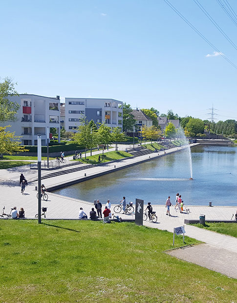 Der Niederfeldsee in Essen-Altendorf mit umliegender Parkanlage, mehreren Passanten und einem Wohnquartier