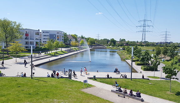Der Niederfeldsee in Essen-Altendorf mit umliegender Parkanlage, mehreren Passanten und einem Wohnquartier