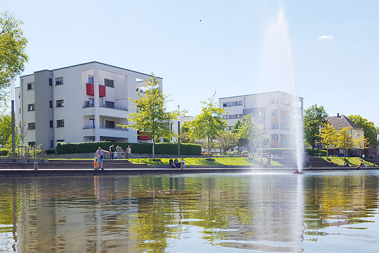 Der Niederfeldsee in Essen-Altendorf mit umliegender Parkanlage, mehreren Passanten und einem Wohnquartier