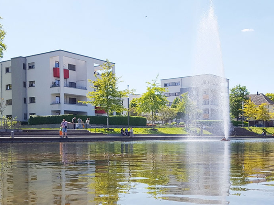 Der Niederfeldsee in Essen-Altendorf mit umliegender Parkanlage, mehreren Passanten und einem Wohnquartier