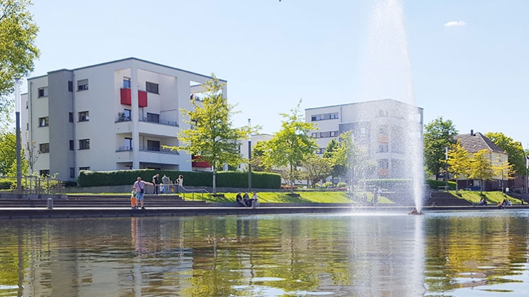 Der Niederfeldsee in Essen-Altendorf mit umliegender Parkanlage, mehreren Passanten und einem Wohnquartier