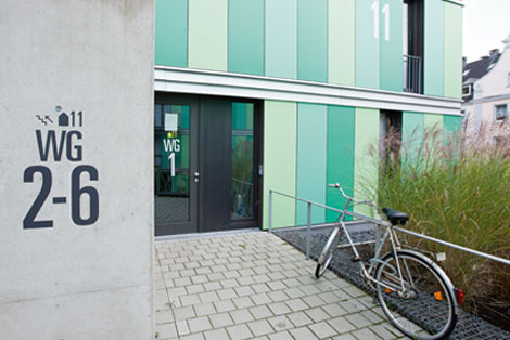 Grüne Fassade und Eingangsbereich eines Studentenwohnheims, davor ein gepflasterter Weg und ein Fahrrad