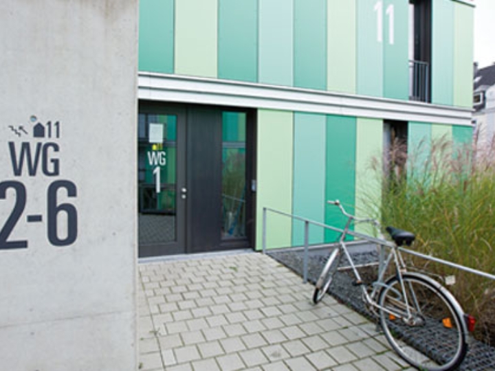 Grüne Fassade und Eingangsbereich eines Studentenwohnheims, davor ein gepflasterter Weg und ein Fahrrad