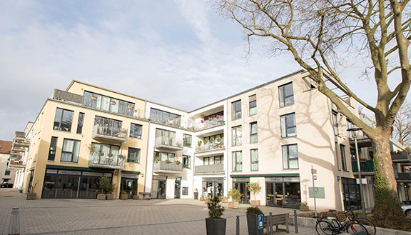 Modernes Wohnquartier mit Innenhof. Im Erdgeschoss ein Cafe, im Hof ein großer Baum und Fahrräder