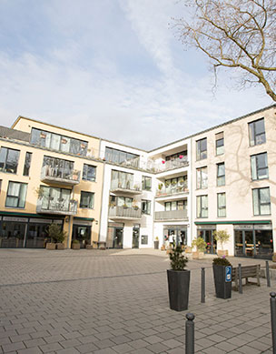 Modernes Wohnquartier mit Innenhof. Im Erdgeschoss ein Cafe, im Hof ein großer Baum und Fahrräder